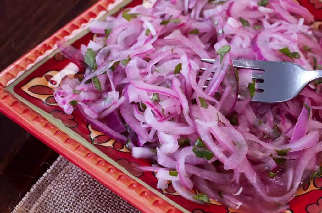 Colorful red pattered plate topped with pink marinated red onions, soaking in their juices with a silver fork