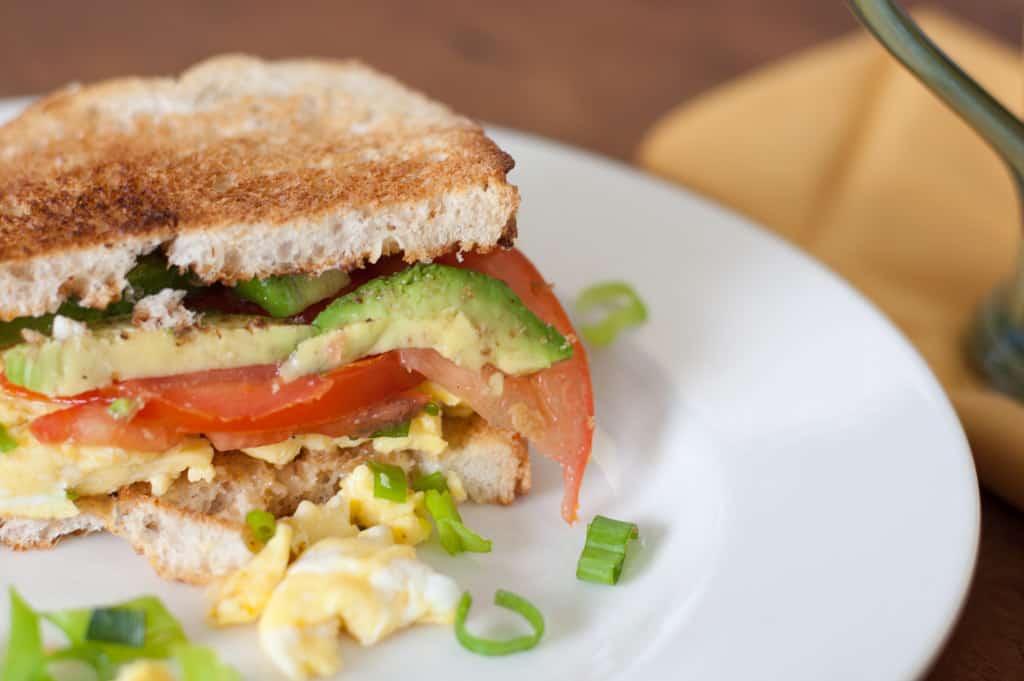 Breakfast sandwich with eggs, avocado, tomatoes, green onions