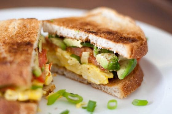 Grown Up Breakfast Sandwich with seasoned eggs, fresh tomatoes, buttery avocado, and green onions served on crusty bread