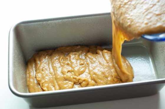 pumpkin banana bread batter being slowly poured into a silver bread pan