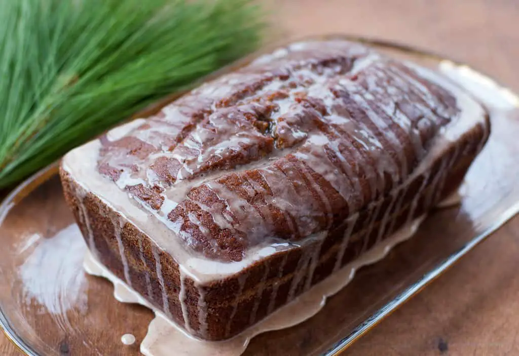 pumpkin banana bread loaf drizzled with cinnamon glaze on a clear platter with pine needles in the background