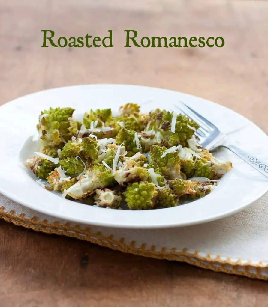 White bowl filled with roasted romanesco with shredded Pecorino Romano on top with a fork and napkin on a wooden tabletop with the test Roasted Romanesco at the top