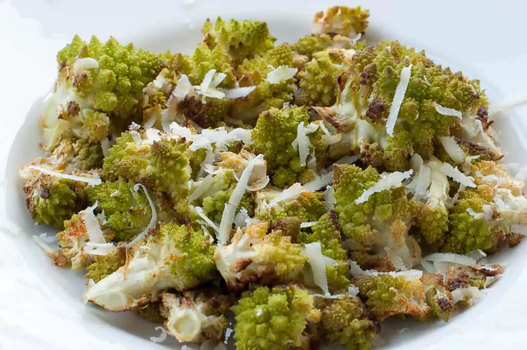 Closeup view of roasted romanesco pieces in a white bowl with shredded Pecorino Romano sprinkled on top