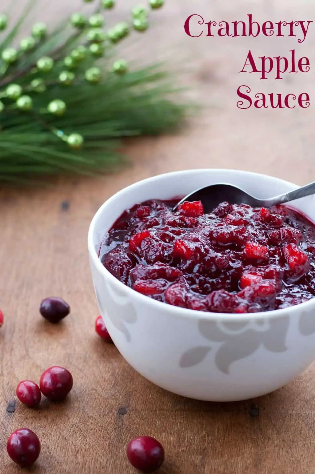 White bowl filled with chunky homemade cranberry sauce with some cranberries, pine needles and holiday decorations in the background