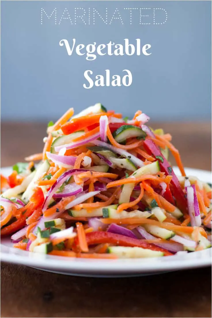 Side view of a thinly sliced vegetables piled high on a white plate with vinaigrette dressing with text Marinated Vegetable Salad