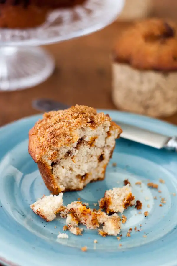 Half eaten cinnamon muffin on a blue plate with a platter of extra muffins in the background