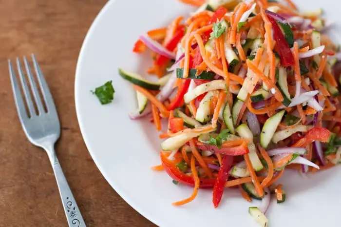 top view of chopped vegetable salad on a white plate with a fork