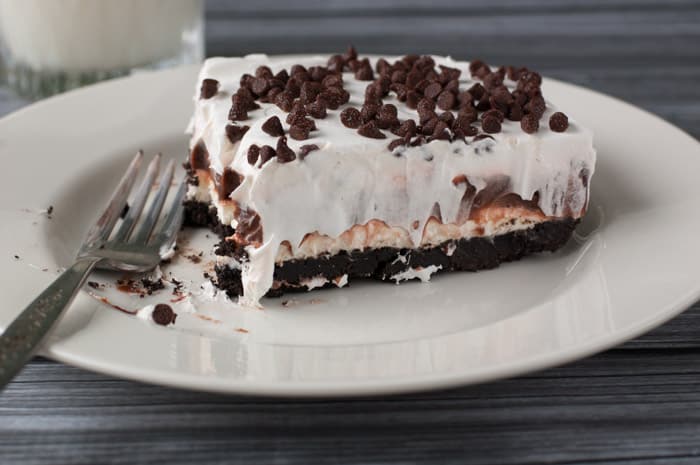 Slice of chocolate lasagna with a bite taken out on a white plate with whipped cream dripping down the sides