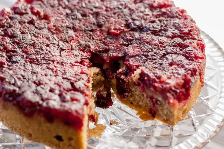 Cranberry Upside Down Cake on a crystal cake plate with a slice taken out