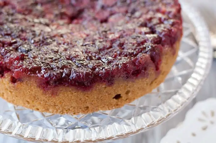 Side view of a whole Cranberry Upside Down Cake on a crystal cake plate with glistening cooked cranberries on top