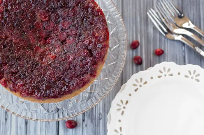 Top view of Cranberry Upside Down Cake on a crystal cake platter with white plates and 3 silver forks