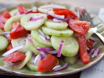 Piles of cucumber, tomatoes, and red onion dressed with a red wine vinaigrette on a green plate