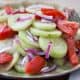 Piles of cucumber, tomatoes, and red onion dressed with a red wine vinaigrette on a green plate