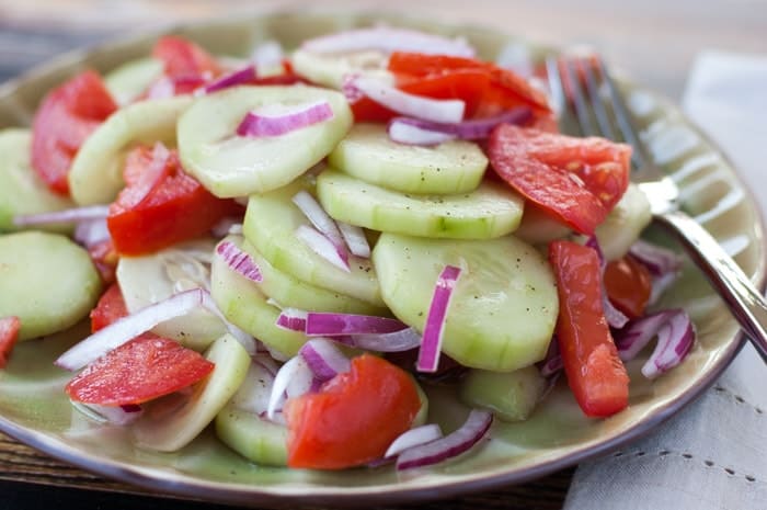 Piles of cucumber, tomatoes, and red onion dressed with a red wine vinaigrette on a green plate