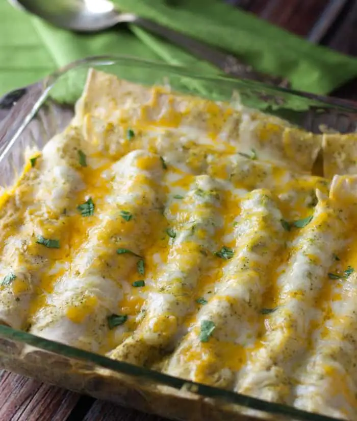Chicken enchiladas in a clear casserole dish smothered with yellow and white lowfat cheese and sprinkled with cilantro