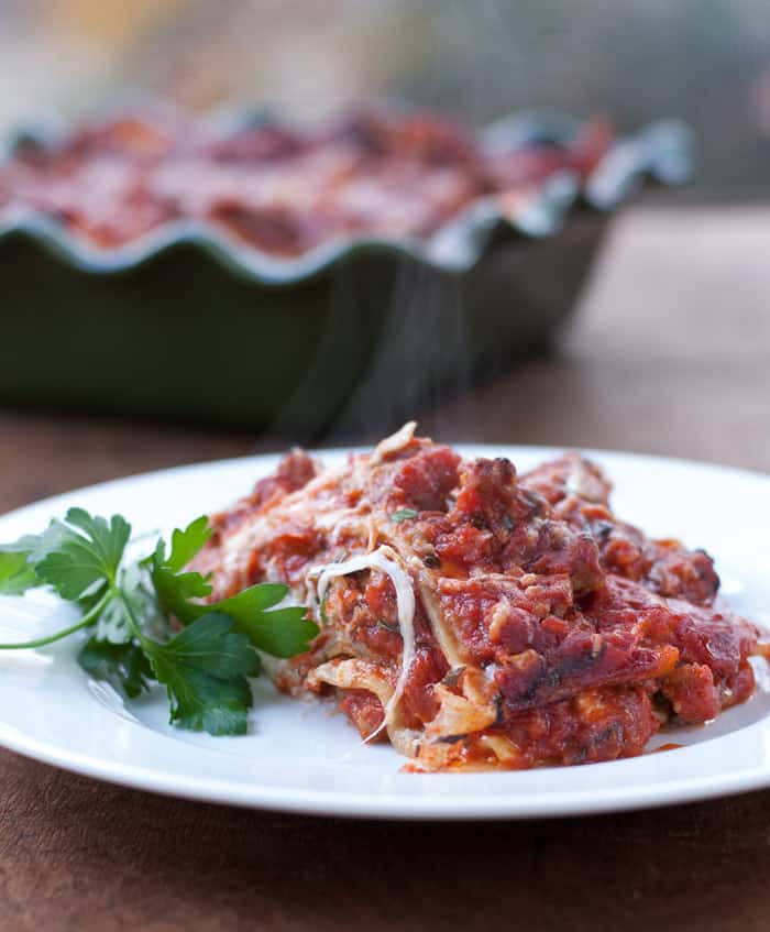 Slice of no boil lasagna on a white plate with a sprig of parsley