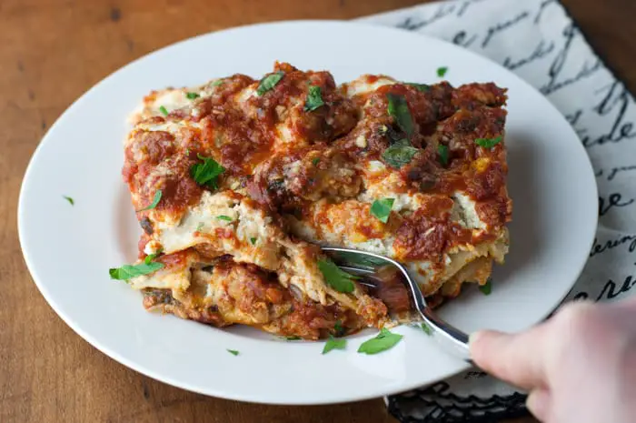 Top view of slice of turkey lasagna with a hand holding a fork to cut off the first bite