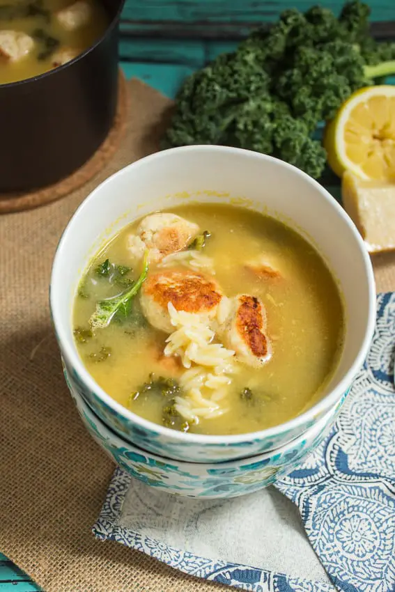 Top view of yellow soup with bits of orzo and chicken meatballs in a blue flowered bowl