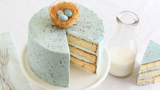 Slice taken out of white cake with thick light blue frosting with brown speckles next to a carafe of milk