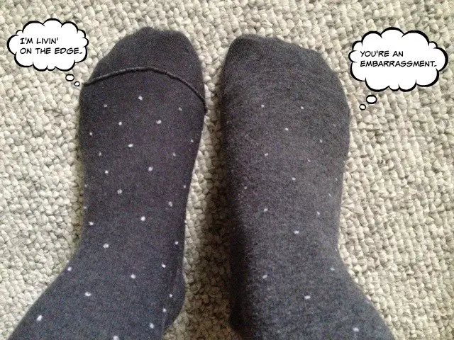 closeup of two feet on carpet both with grey socks with white polka dots. One sock is inside out.