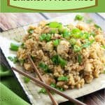 Large portion of spicy chicken fried rice topped with chopped green onions on a beige square plate with dark brown wooden chopsticks