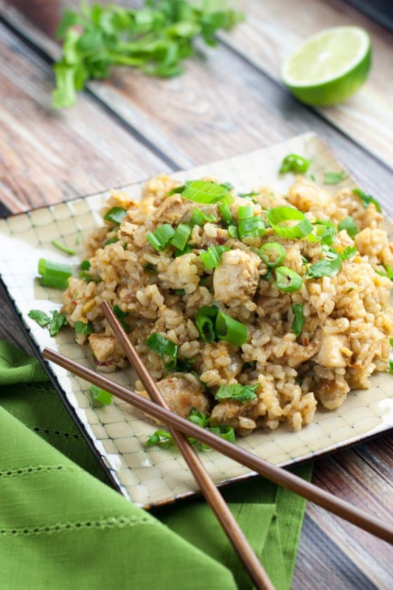 top view of spicy chicken fried rice topped with green onions on a square beige plate with brown wooden chopsticks