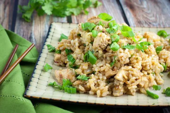 Heaping pile of spicy chicken fried rice on top of a beige and black geometric square plate with chopsticks nearby