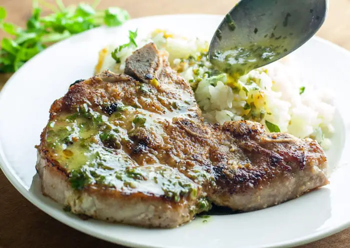 A spoon ladling honey lime cilantro sauce on the top of a nicely seared pork chop with a side of white rice 