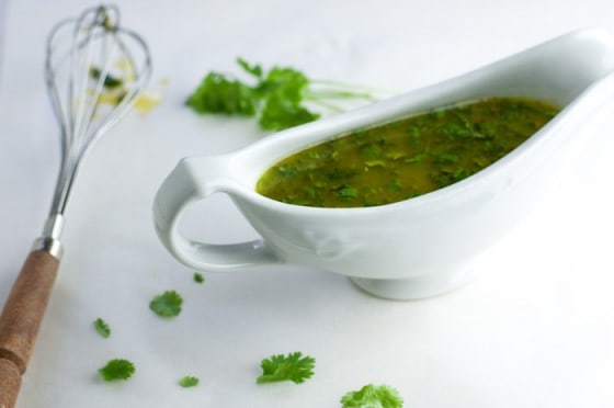 Side view of white gravy boat filled with honey lime cilantro sauce and silver whisk with wood handle next to it