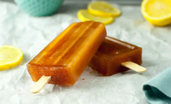 side view of two tea popsicles stacked on top of each other on parchment paper with lemon slices around them