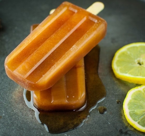 two tea colored popsicles stacked on top of each other partially melting with two lemon slices