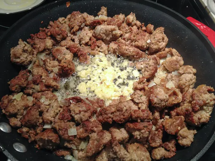 nonstick skillet with broken meatballs fully cooked, onions added and center filled with sizzling garlic
