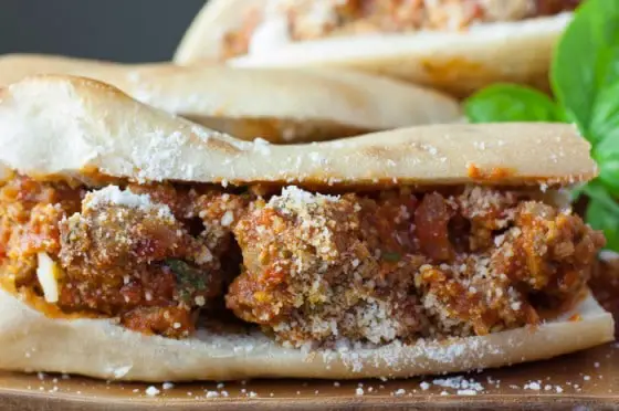 Closeup of meatball sub sandwich filled with moist meatballs covered in sauce and sprinkled with Pecorino Romano cheese
