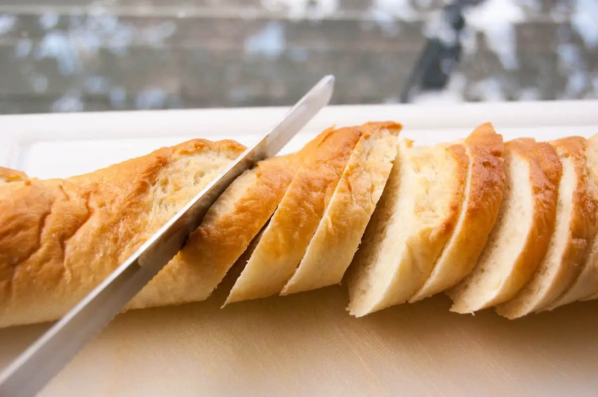 Long French baguette being sliced with a long serrated bread knife