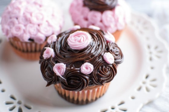 Closeup of strawberry and fudge cupcake with chocolate and strawberry frosting rosettes on a white plate