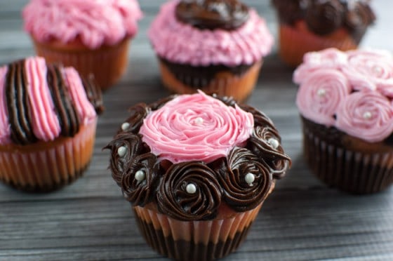 Closeup of pink and brown swirled frosting cupcake with white pearl candies with other cupcakes in the background