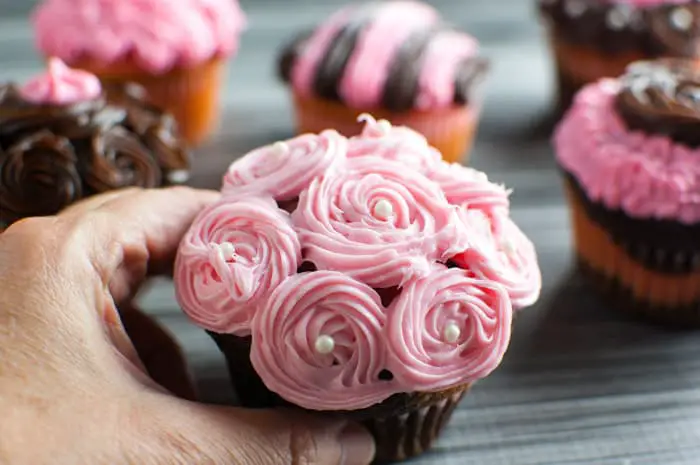 Hand holding a chocolate cupcakes with pink frosting with rosettes and pearl candies