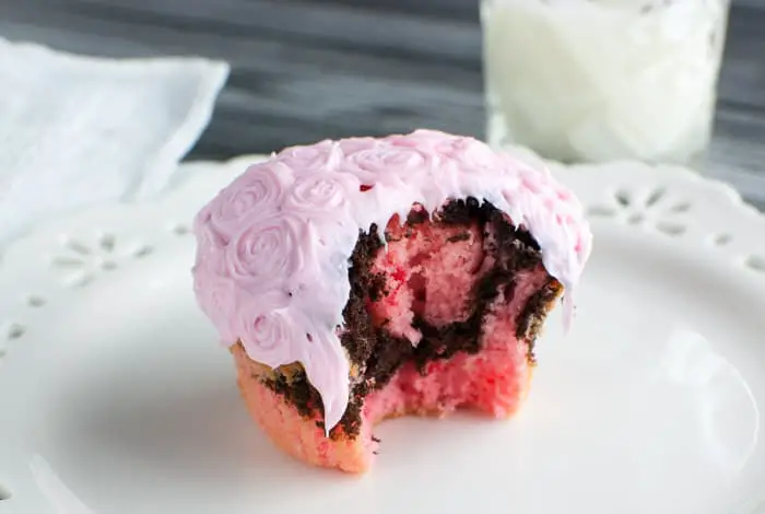 Strawberry and fudge cupcake with pink frosting with a huge bite taken out on a white plate