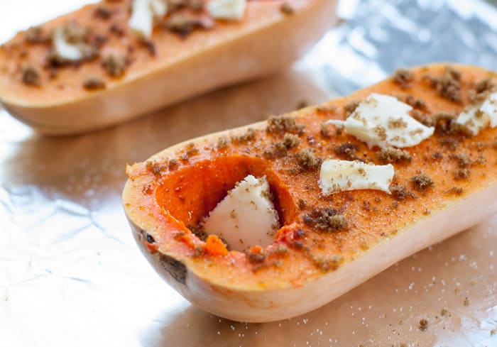 Butternut squash cut in half with sprinkled brown sugar and cinnamon on top with little pats of butter on foil