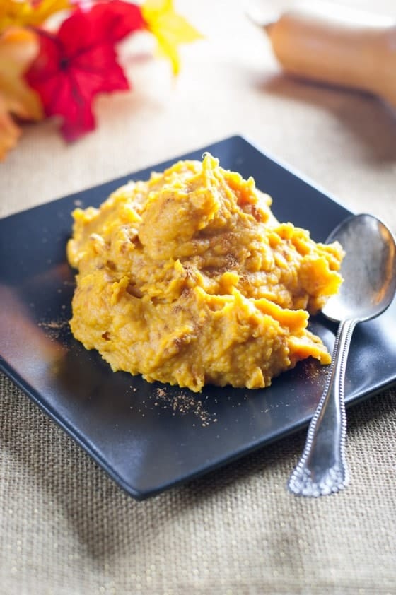 Mashed Butternut Squash on a black plate with cinnamon sprinkled on top with fall leaves blurred in the background