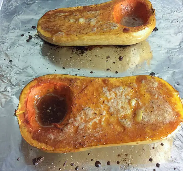 Two halves of butternut squash on tinfoil completely roasted with melted butter on top