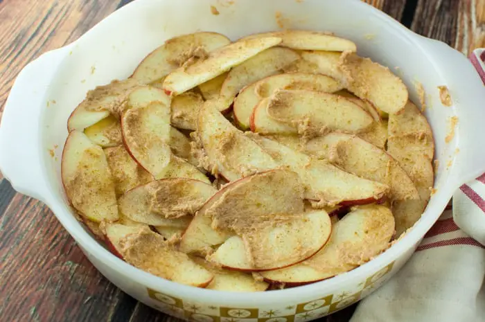 Layers of sliced red apples and butter mixture in a vintage white baking dish