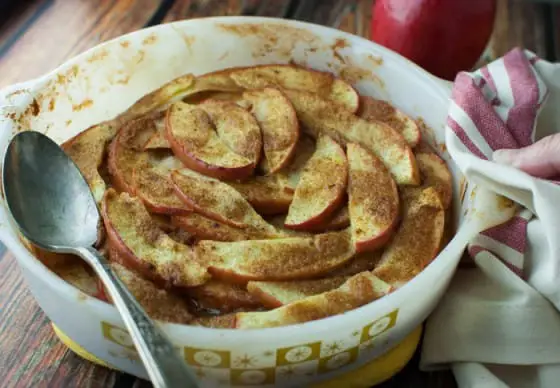 Fully cooked baked apple slices in a white baking dish with a silver serving spoon