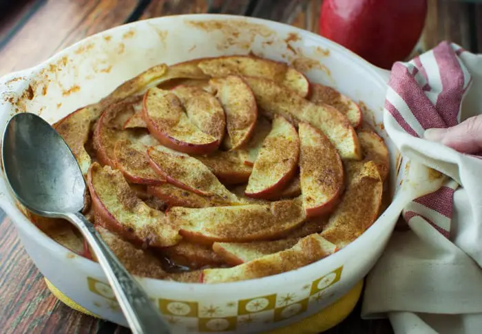 Fully cooked baked apple slices in a white baking dish with a silver serving spoon