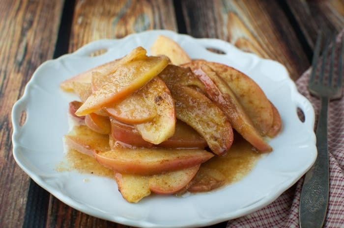 White plate topped with baked apples slices and covered with buttery apple pie sauce