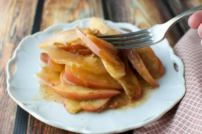 Saucy sliced baked apples on a white plate with a fork grabbing a bite