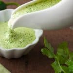 White gravy boat filled with thick Peruvian green sauce being poured into a white ramiken