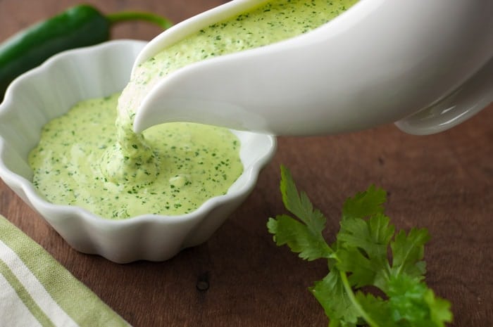 White gravy boat filled with thick Peruvian green sauce being poured into a white ramiken