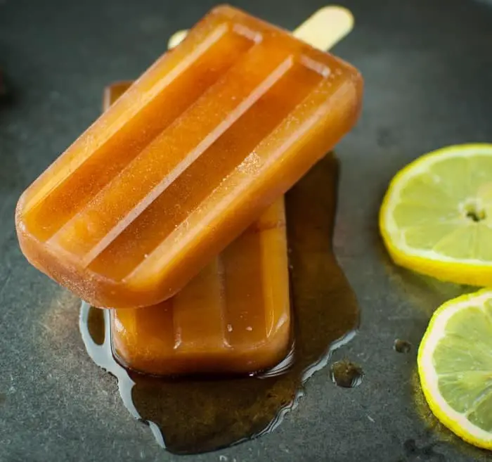 Two tea colored popsicles on top of each other slightly melted with some lemon slices nearby