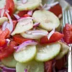 Sliced cucumbers, red onions, and tomatoes dressed with vinaigrette on a green plate with a fork